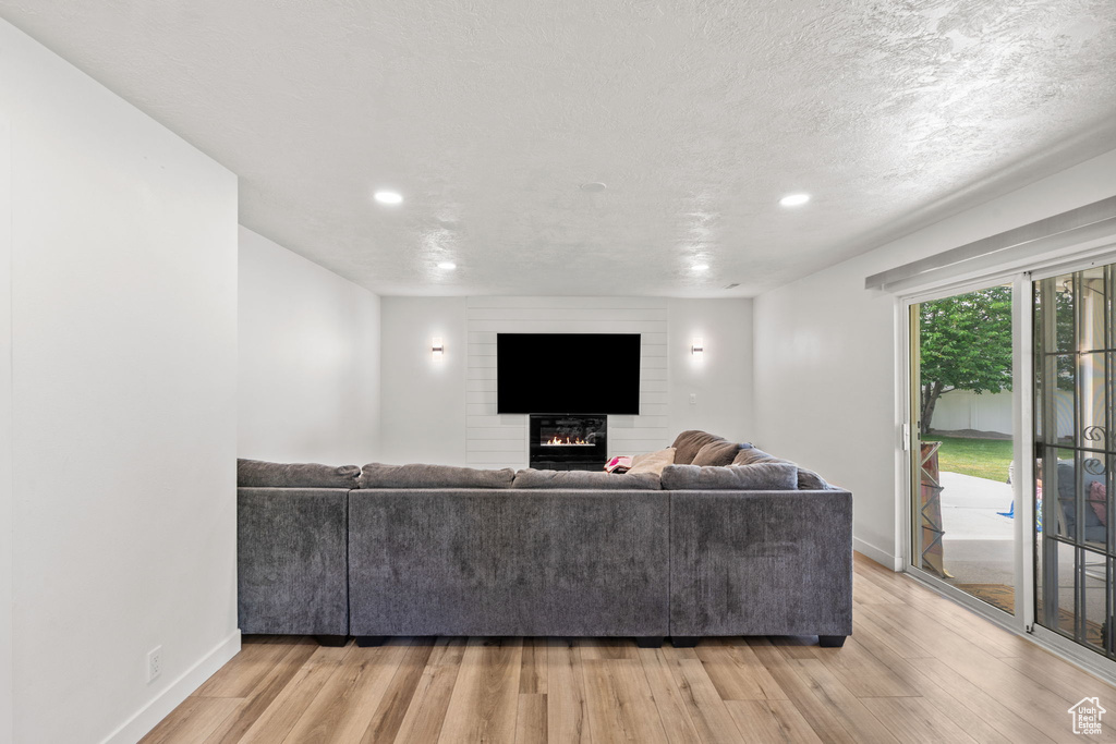 Living room with light wood-type flooring, a large fireplace, and recessed lighting