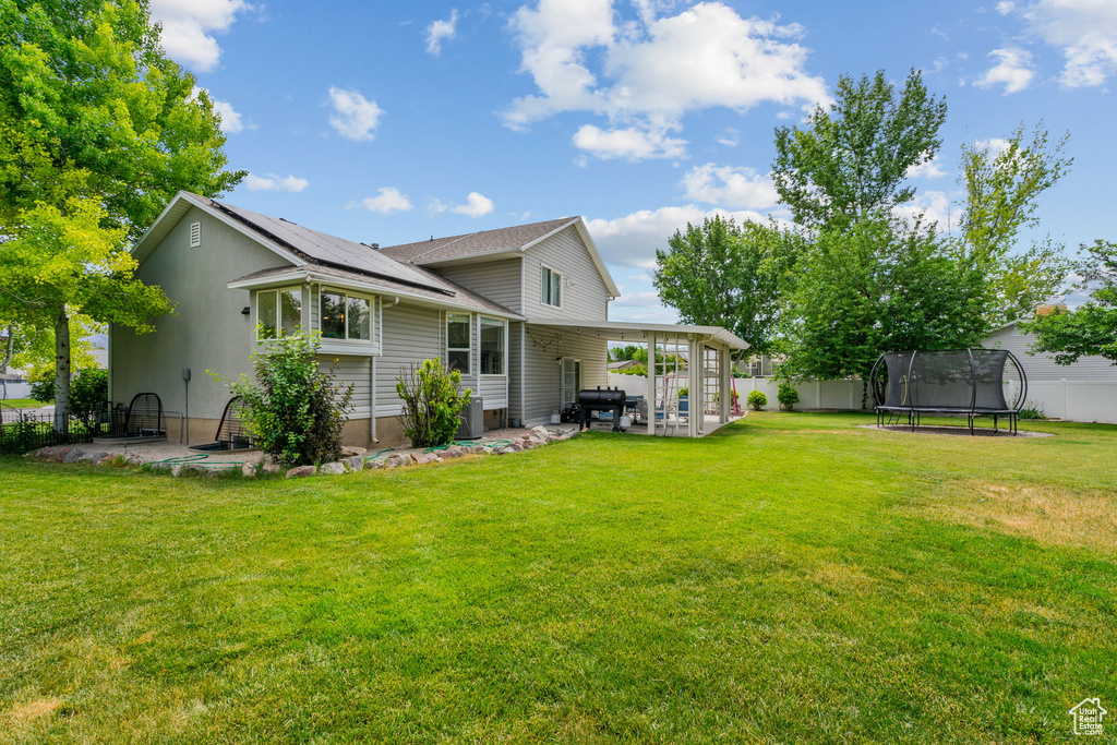 Back of house featuring a trampoline, a patio, a fenced backyard, and solar panels