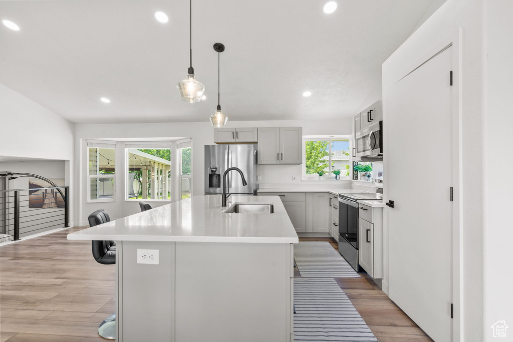Kitchen with appliances with stainless steel finishes, a center island with sink, a breakfast bar area, recessed lighting, and light countertops