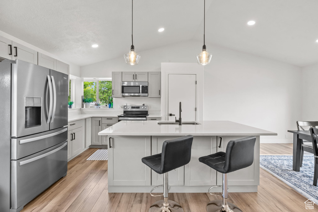 Kitchen featuring appliances with stainless steel finishes, vaulted ceiling, light countertops, light wood-style floors, and a kitchen bar