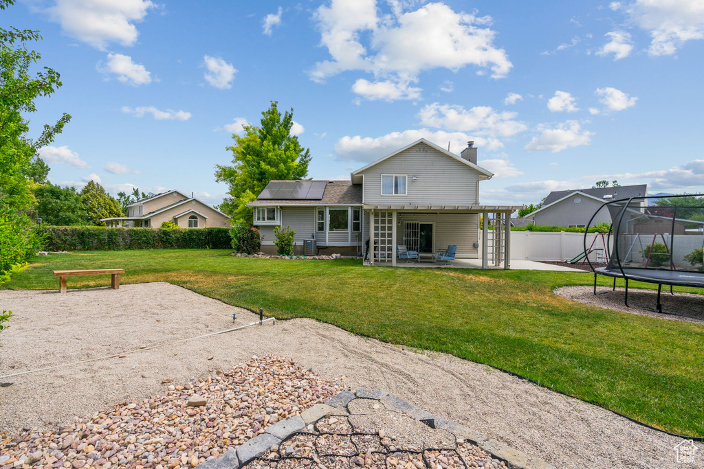 Rear view of property featuring a trampoline, a patio, solar panels, a chimney, and a fenced backyard