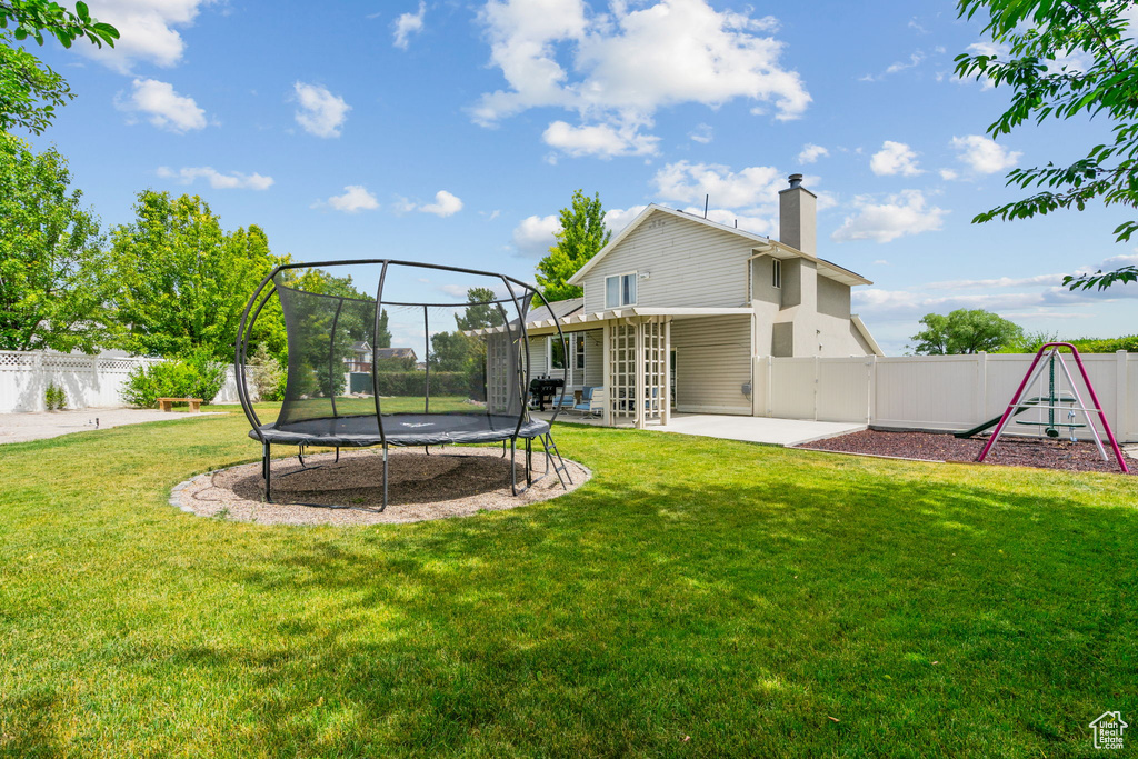 Back of house featuring a trampoline, a chimney, a patio, a playground, and a fenced backyard