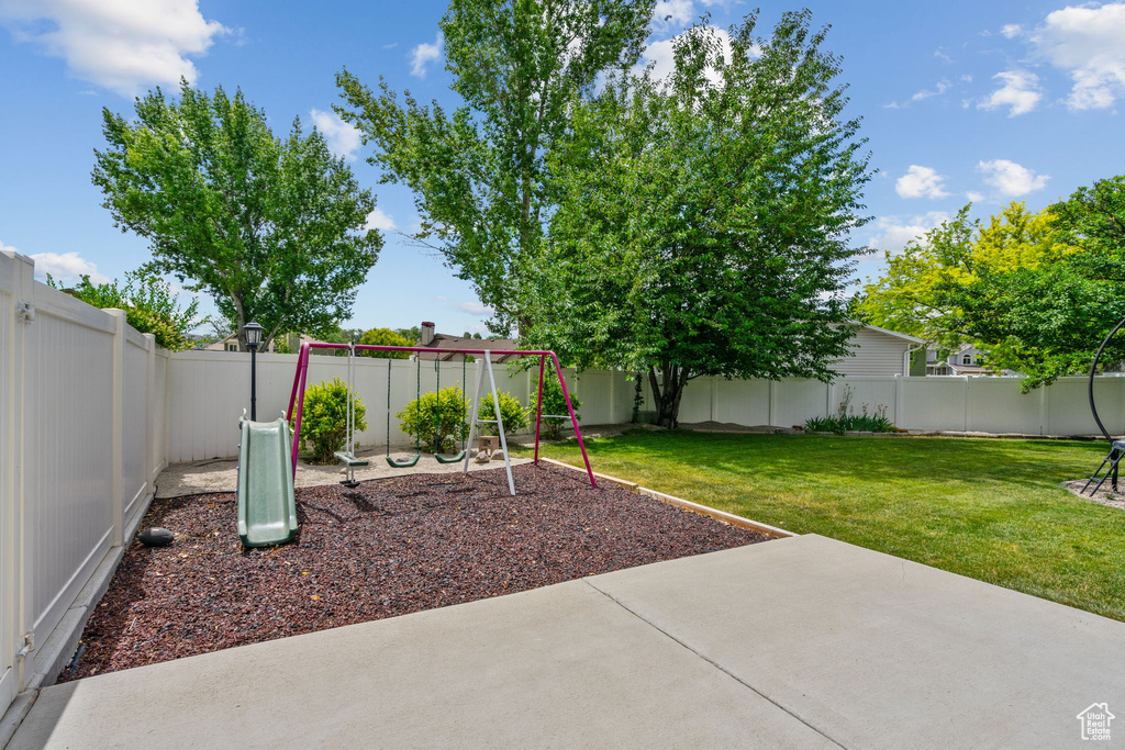 Fenced backyard featuring a playground and a patio