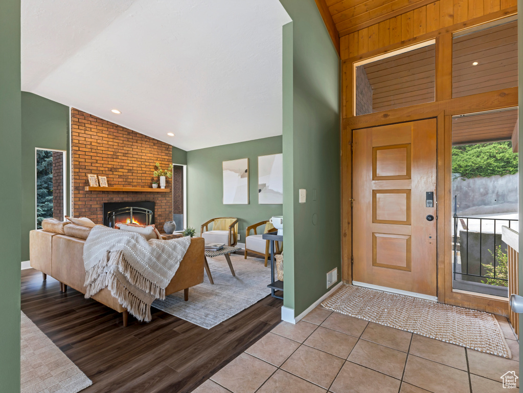 Foyer with lofted ceiling, light wood-type flooring, a fireplace, and wooden walls