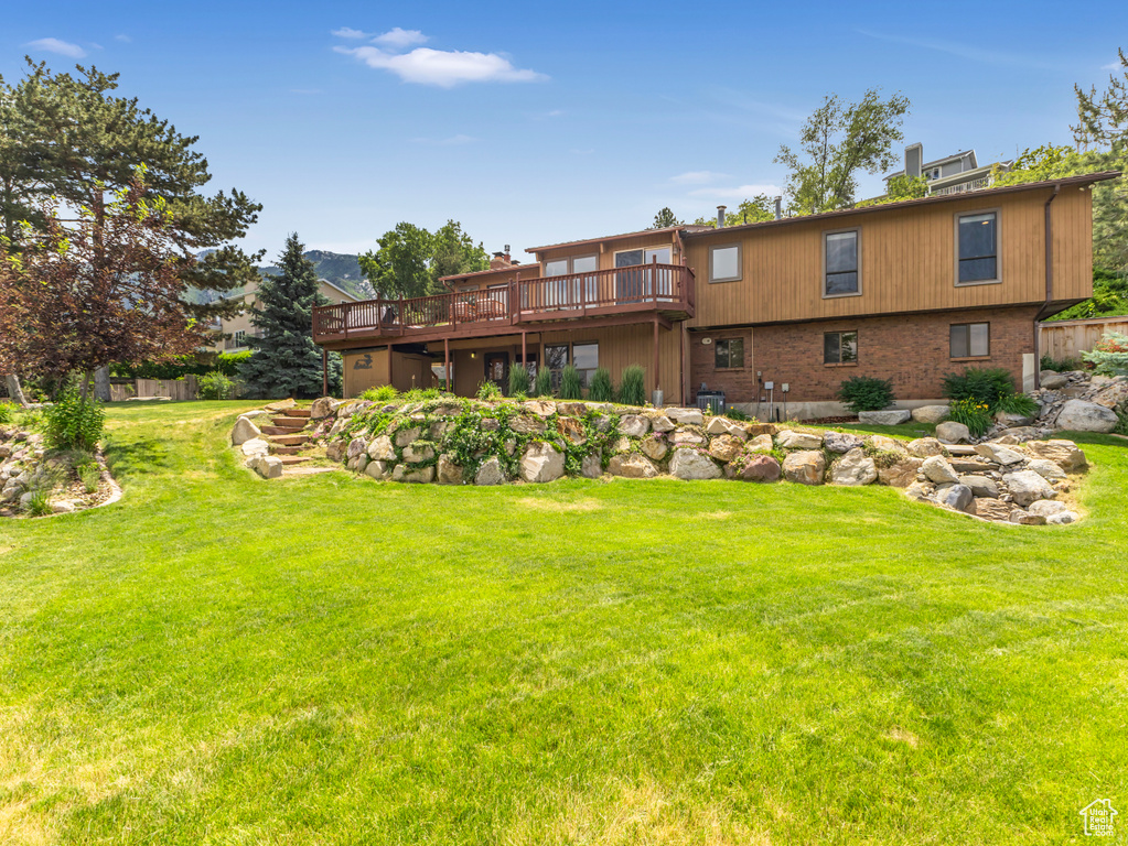 Rear view of property with a wooden deck, a yard, a chimney, and brick siding