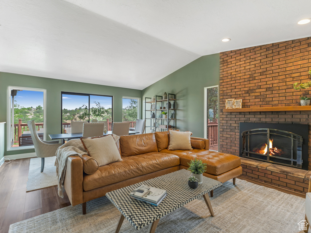 Living room with lofted ceiling, wood finished floors, a brick fireplace, and recessed lighting