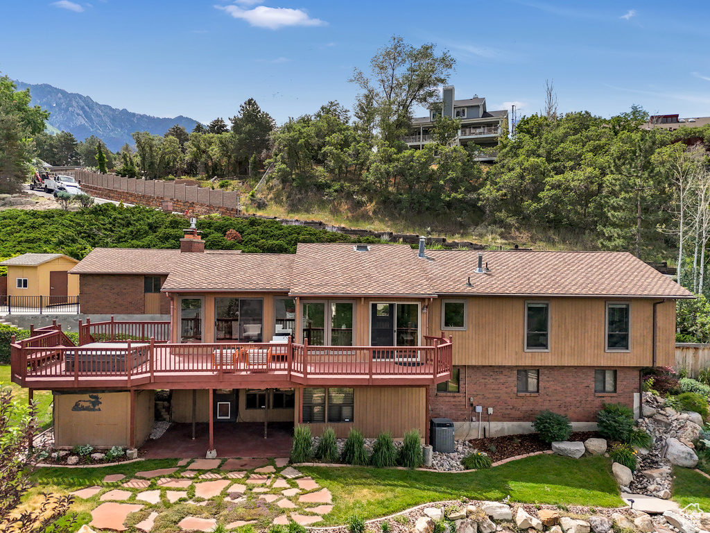 Back of property featuring a deck with mountain view, a patio, a chimney, and a lawn