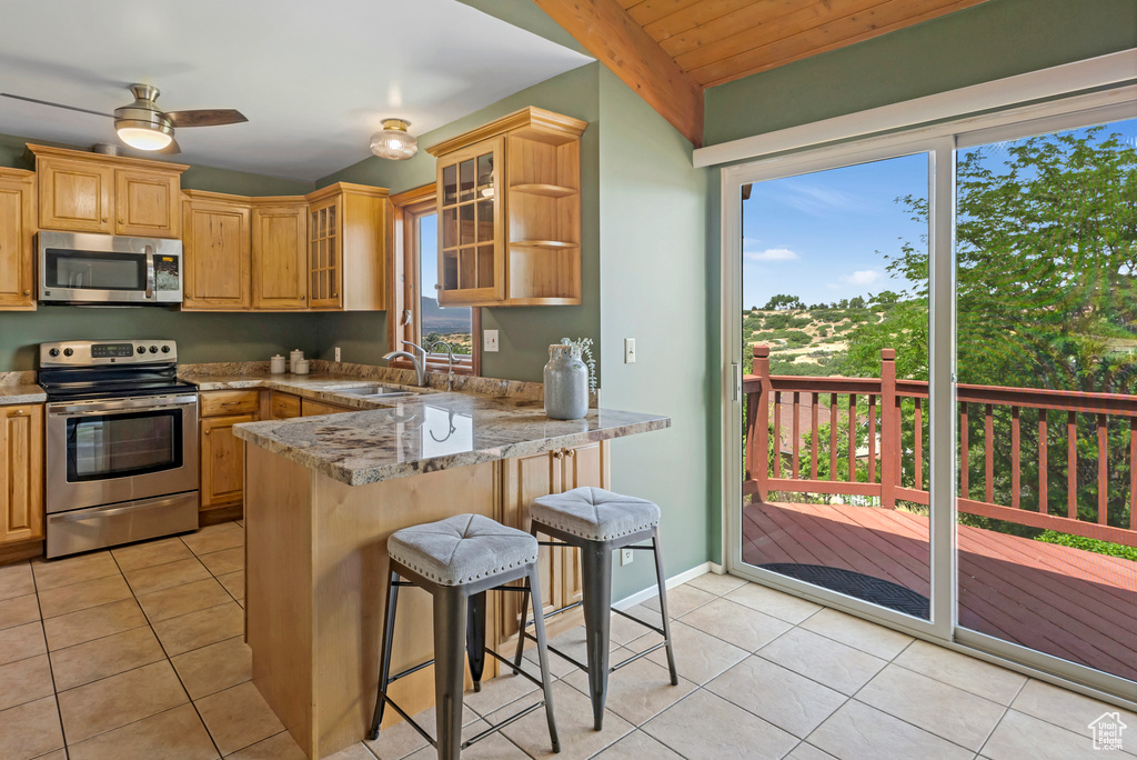 Kitchen featuring appliances with stainless steel finishes, a peninsula, light tile patterned floors, a kitchen breakfast bar, and wooden ceiling