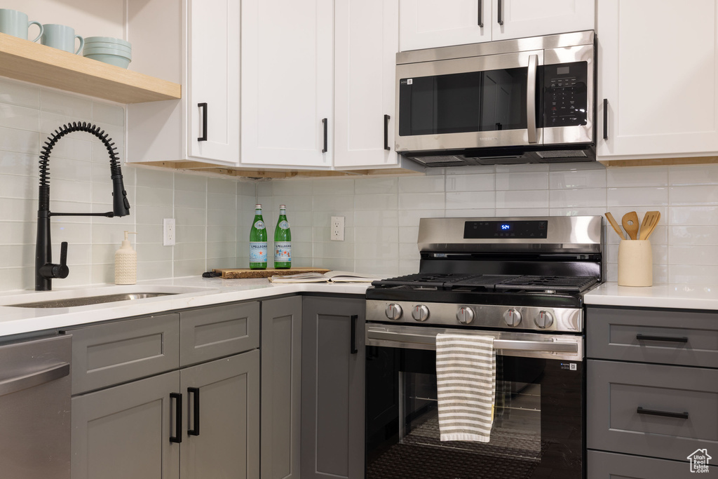 Kitchen featuring stainless steel appliances, gray cabinetry, light countertops, backsplash, and open shelves