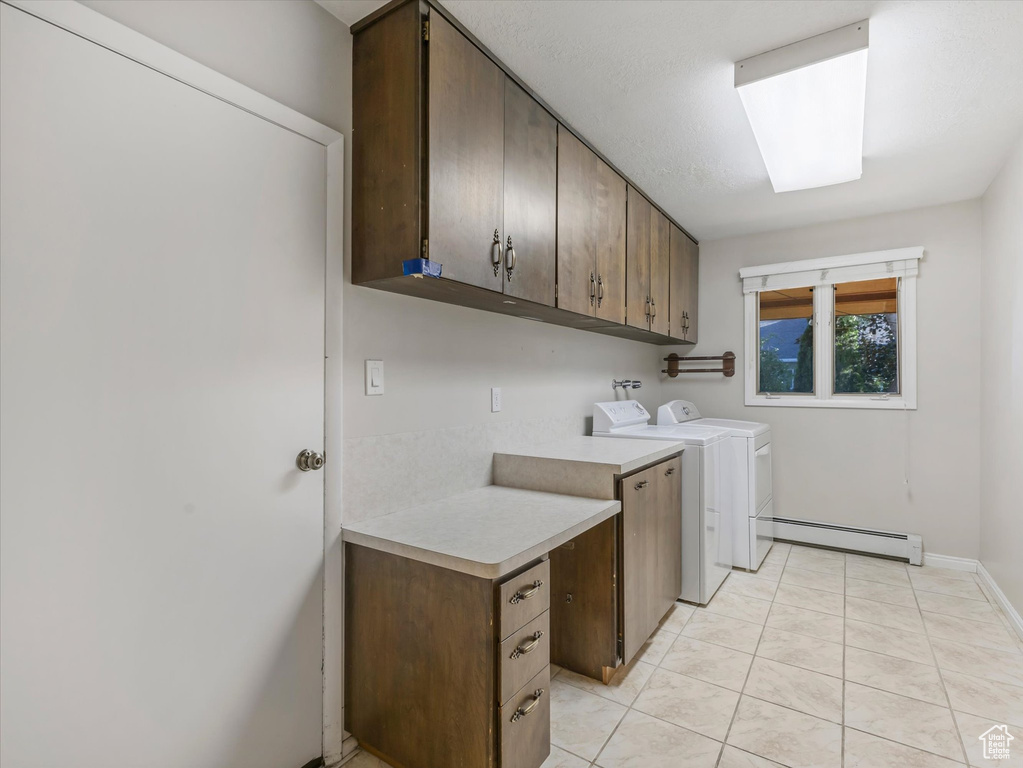 Laundry area with cabinet space, a baseboard radiator, washer and clothes dryer, and light tile patterned floors