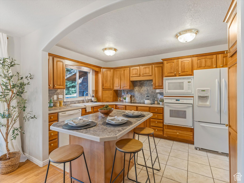 Kitchen with white appliances, light countertops, a kitchen breakfast bar, backsplash, and arched walkways