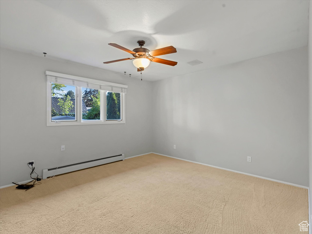 Spare room featuring a baseboard heating unit, ceiling fan, and carpet