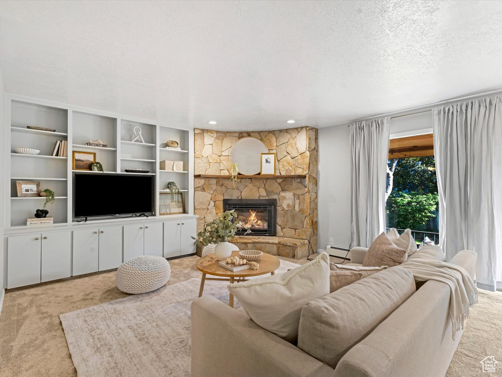 Living area with light colored carpet, a baseboard heating unit, a stone fireplace, and a textured ceiling