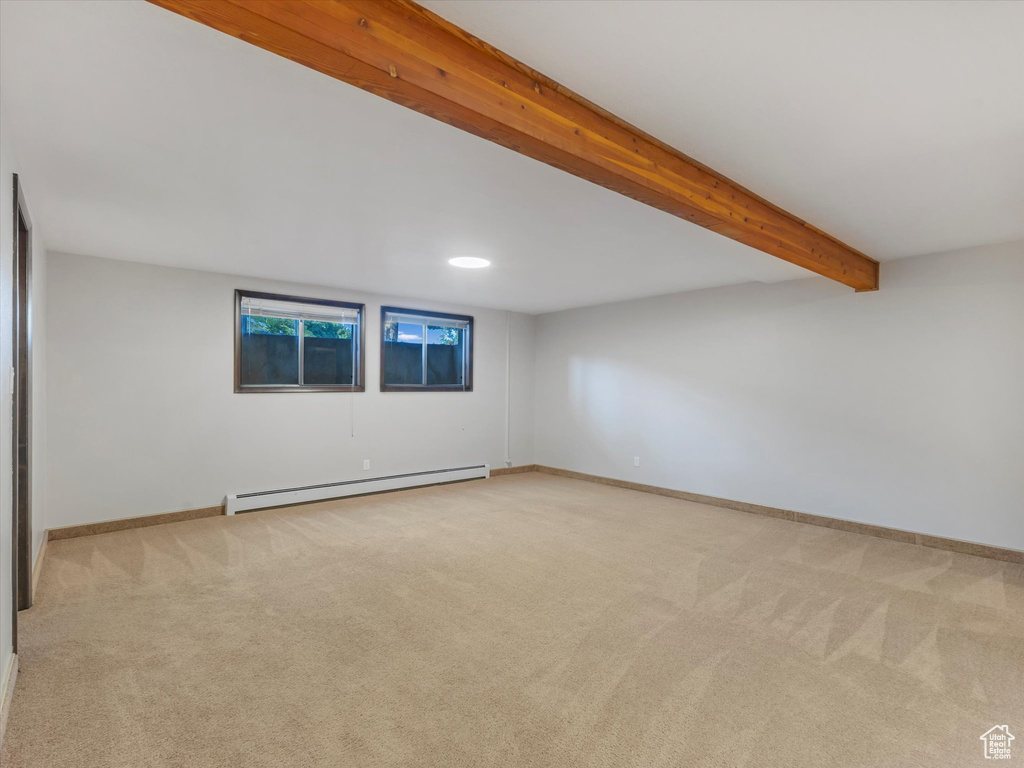 Spare room with a baseboard heating unit, carpet flooring, and beamed ceiling
