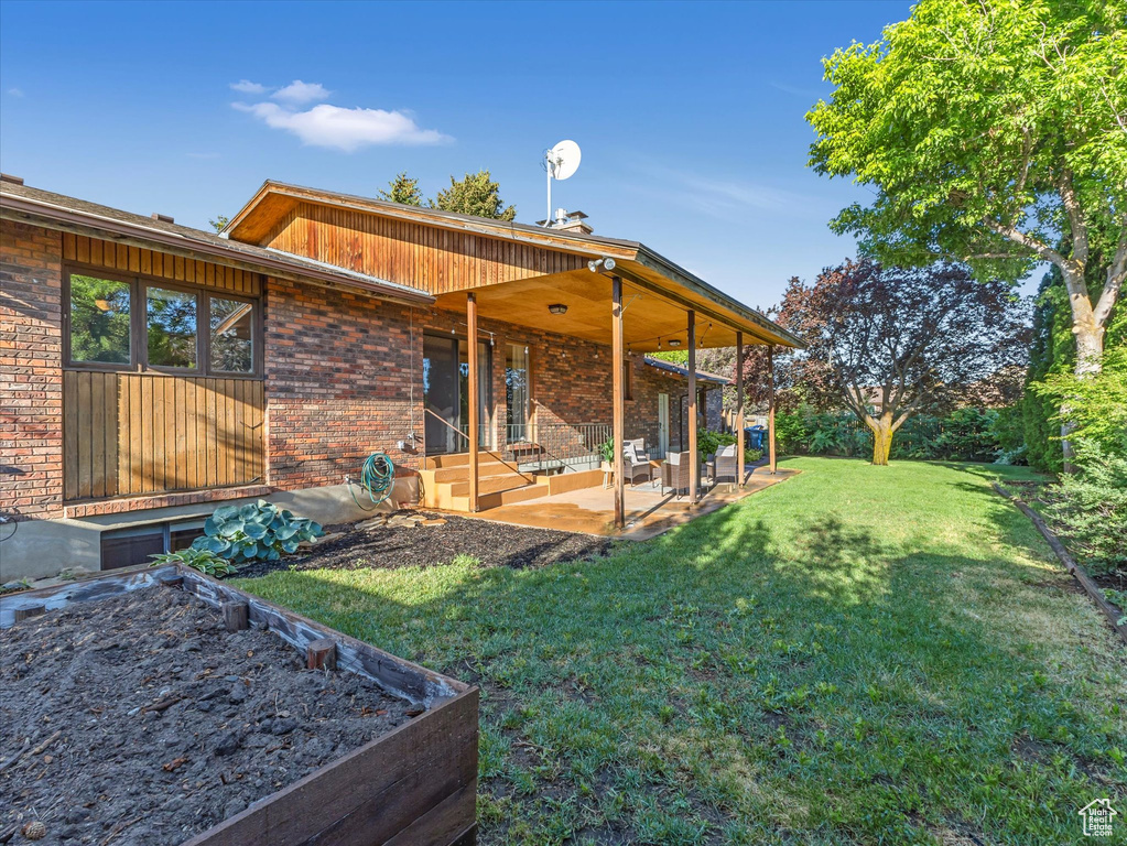 Back of house featuring a patio, a lawn, and brick siding