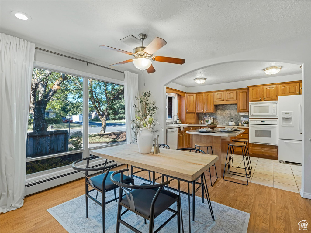 Dining area with a ceiling fan, light wood-style flooring, a baseboard radiator, and arched walkways