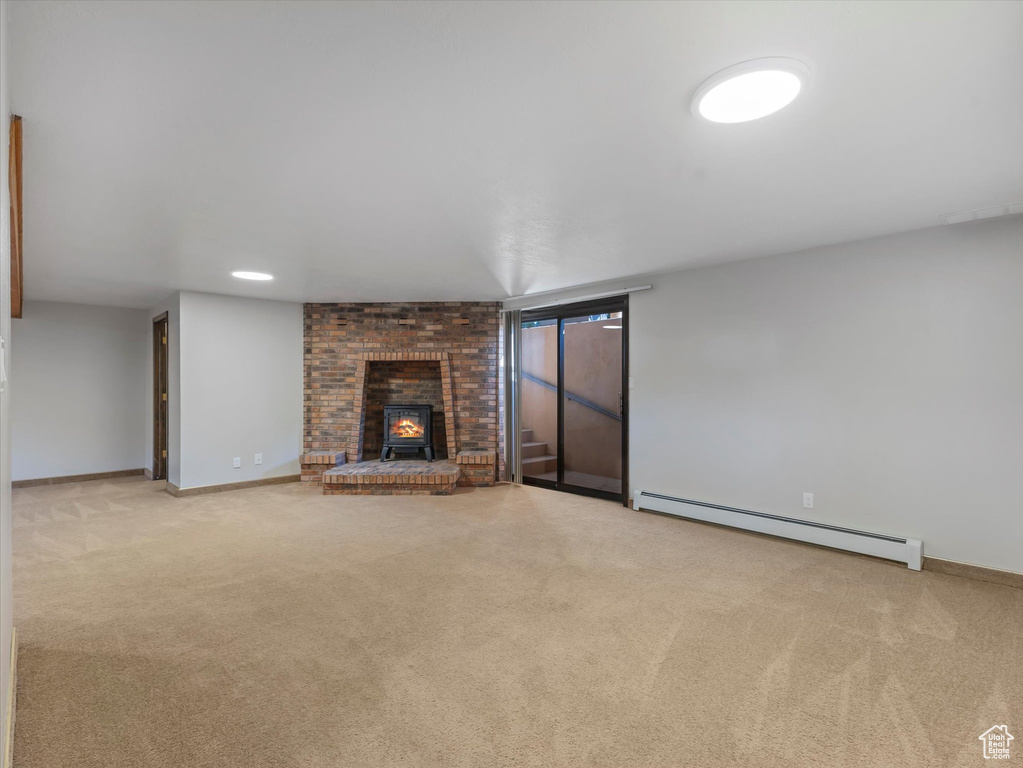 Unfurnished living room with baseboard heating, a brick fireplace, and carpet