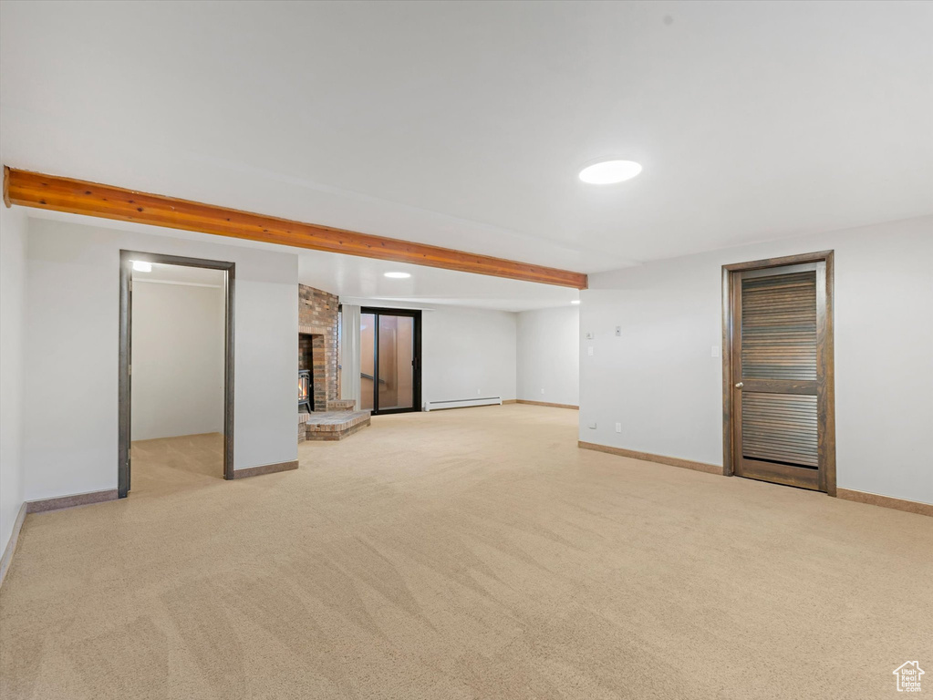 Finished below grade area featuring baseboard heating, light colored carpet, and a brick fireplace