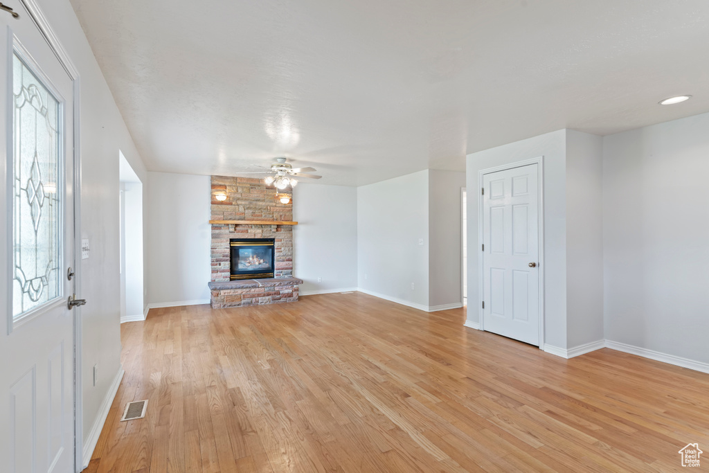 Unfurnished living room featuring light wood-type flooring, a ceiling fan, and a large fireplace