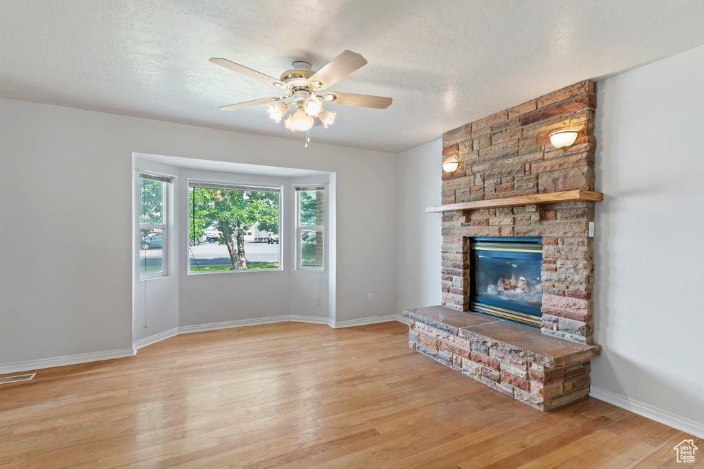 Unfurnished living room with a ceiling fan, light wood-type flooring, a fireplace, and a textured ceiling