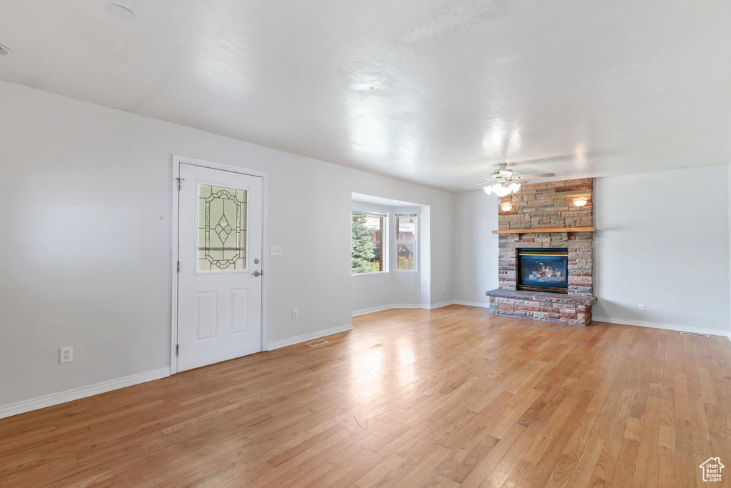 Unfurnished living room with light wood finished floors, a large fireplace, and ceiling fan