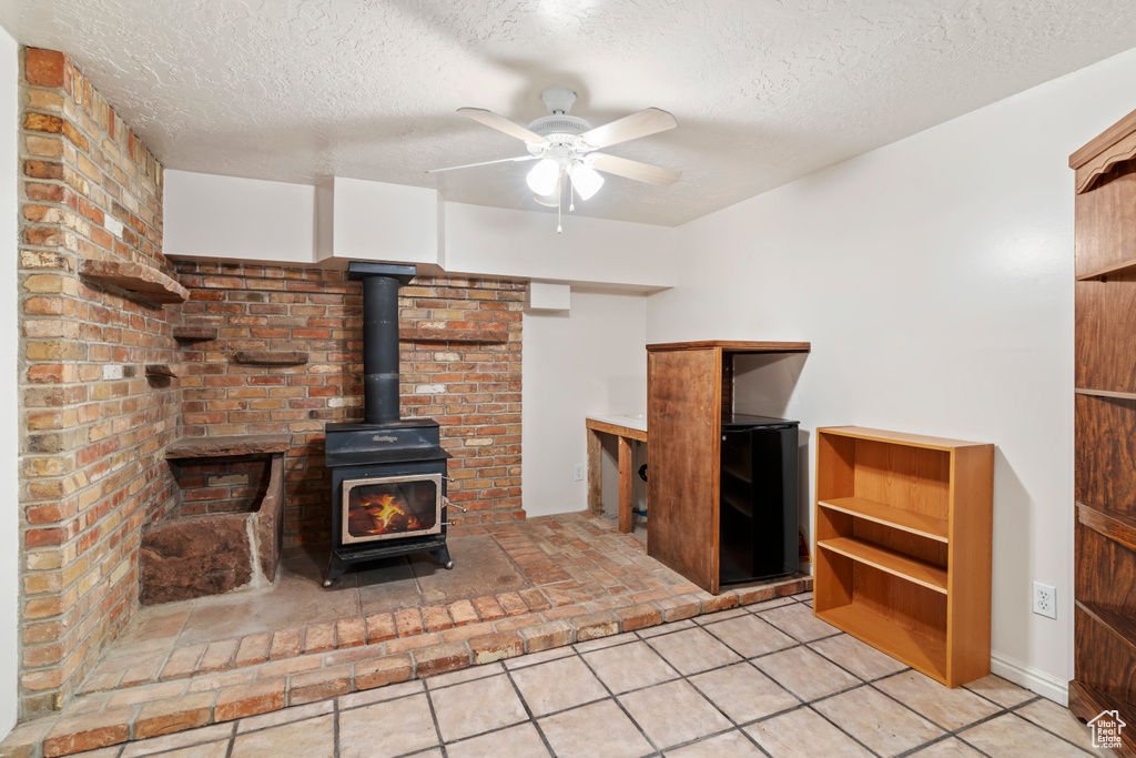 Unfurnished living room featuring a textured ceiling, a ceiling fan, a wood stove, and light tile patterned floors