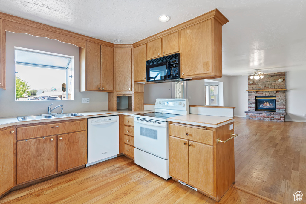 Kitchen featuring white appliances, a peninsula, light wood-type flooring, a fireplace, and light countertops