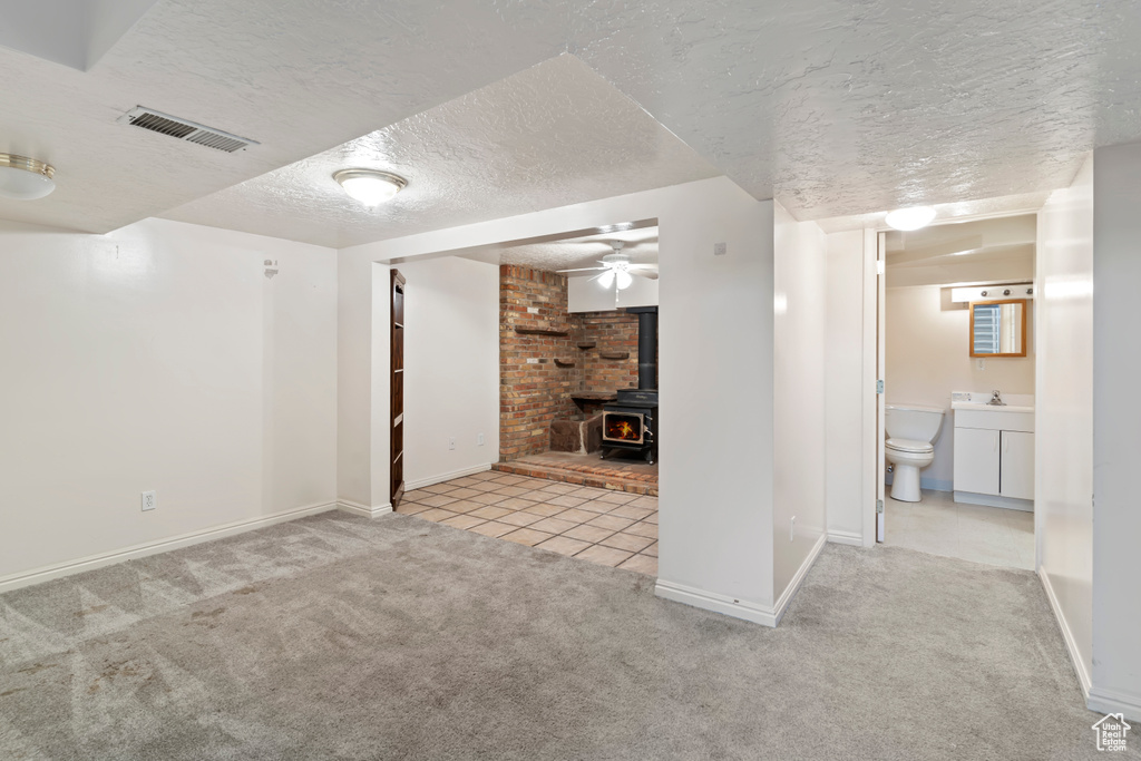 Unfurnished living room with a wood stove, carpet, a textured ceiling, a ceiling fan, and tile patterned floors