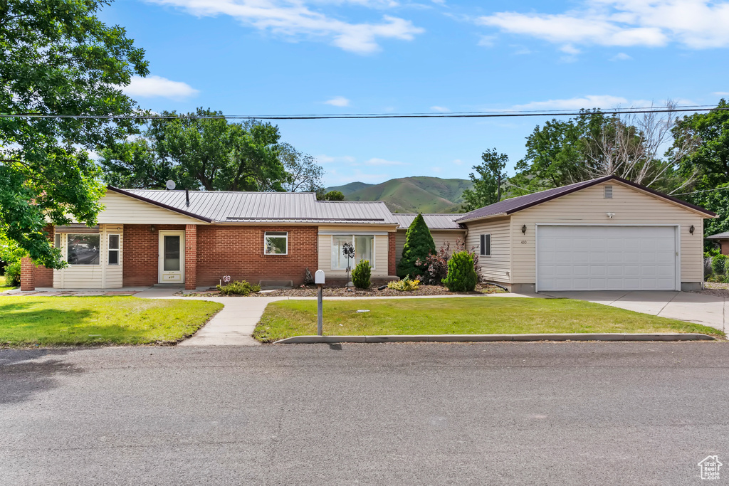 Single story home featuring a garage, a mountain view, a front lawn, brick siding, and a metal roof