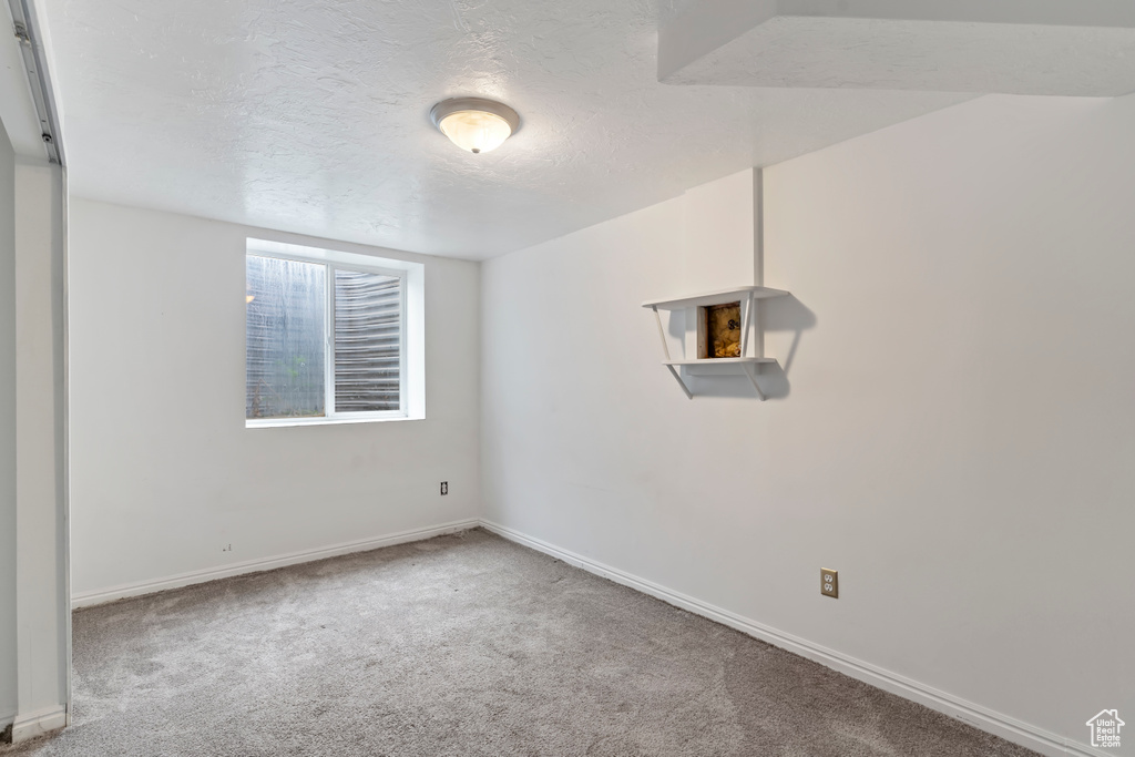Carpeted empty room featuring a textured ceiling and baseboards