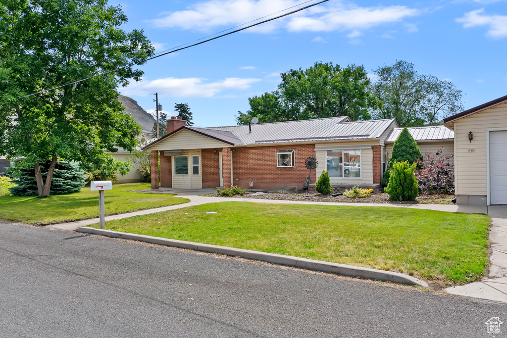 View of front of property featuring brick siding, a front yard, a chimney, and a metal roof