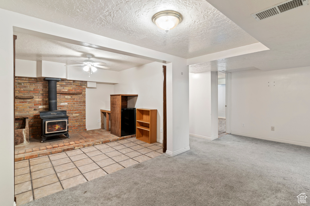Unfurnished living room with carpet, a textured ceiling, a wood stove, ceiling fan, and tile patterned flooring