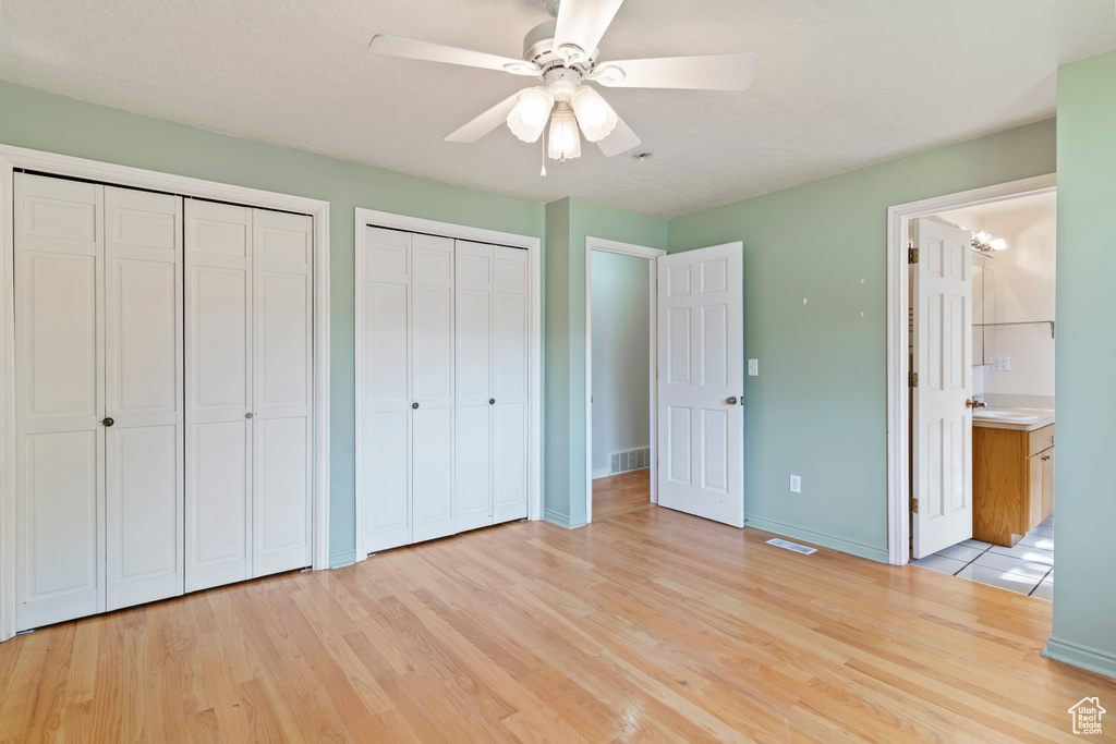 Unfurnished bedroom featuring multiple closets, light wood-type flooring, ensuite bath, and a ceiling fan