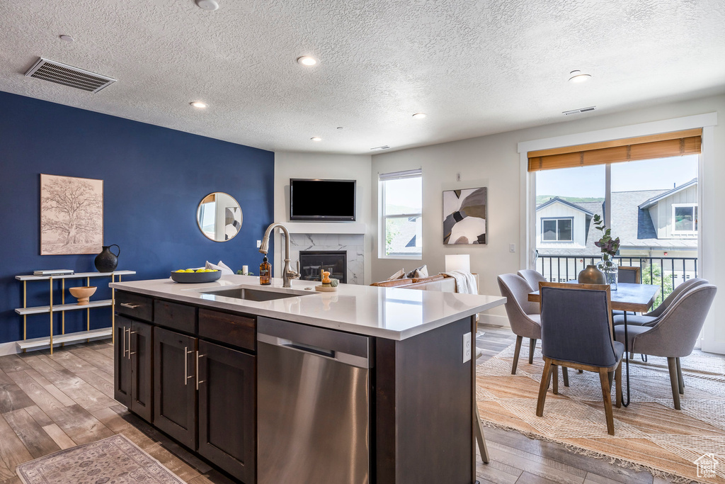 Kitchen with dishwasher, a textured ceiling, light wood-style flooring, light countertops, and a high end fireplace