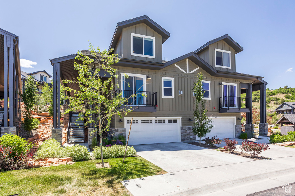 View of front of home with board and batten siding, an attached garage, stone siding, and driveway