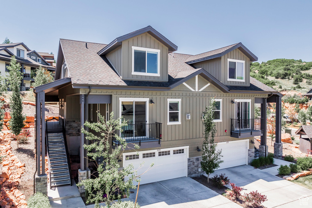 View of front facade featuring roof with shingles, an attached garage, concrete driveway, board and batten siding, and stone siding