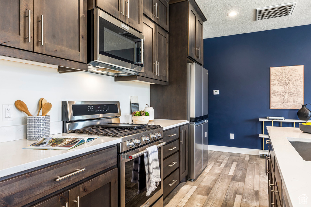 Kitchen featuring appliances with stainless steel finishes, dark brown cabinets, light countertops, light wood-style floors, and a textured ceiling