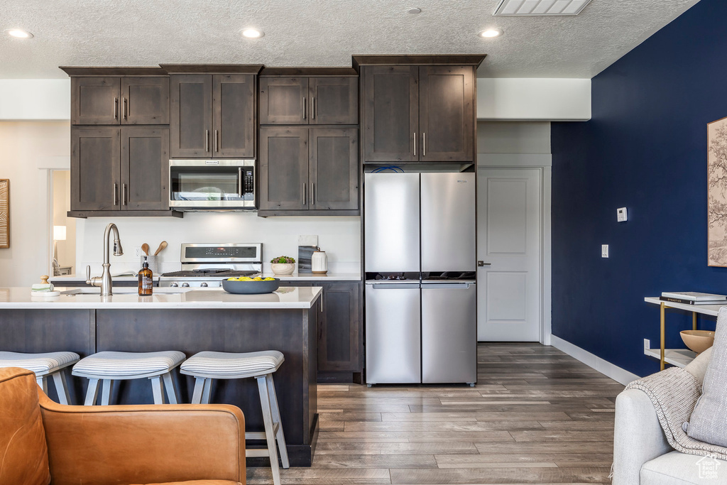 Kitchen with appliances with stainless steel finishes, dark brown cabinets, a textured ceiling, dark wood-style flooring, and light countertops