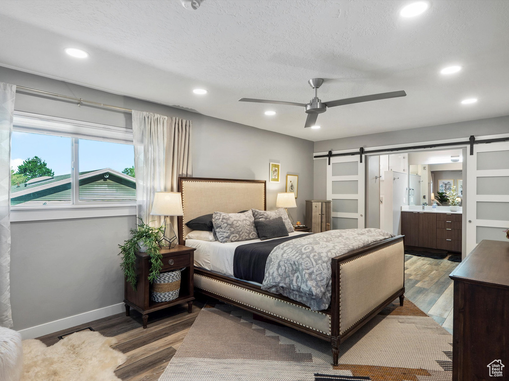 Bedroom featuring a barn door, recessed lighting, wood finished floors, and connected bathroom