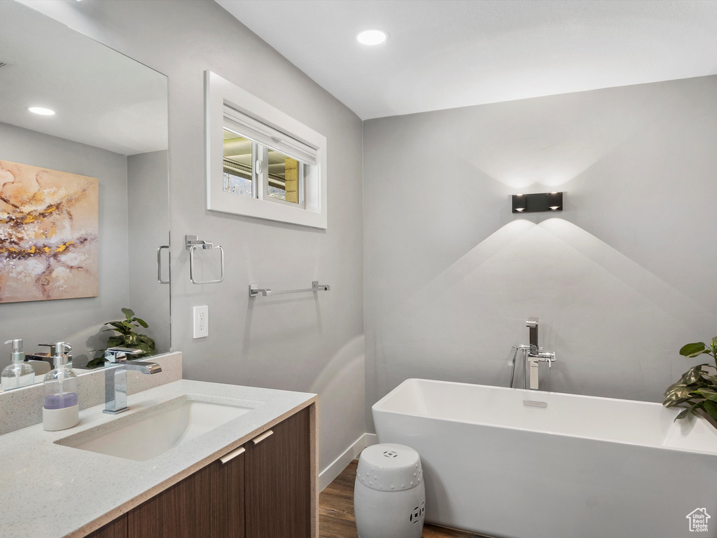 Full bathroom featuring a freestanding bath, wood finished floors, vanity, and recessed lighting