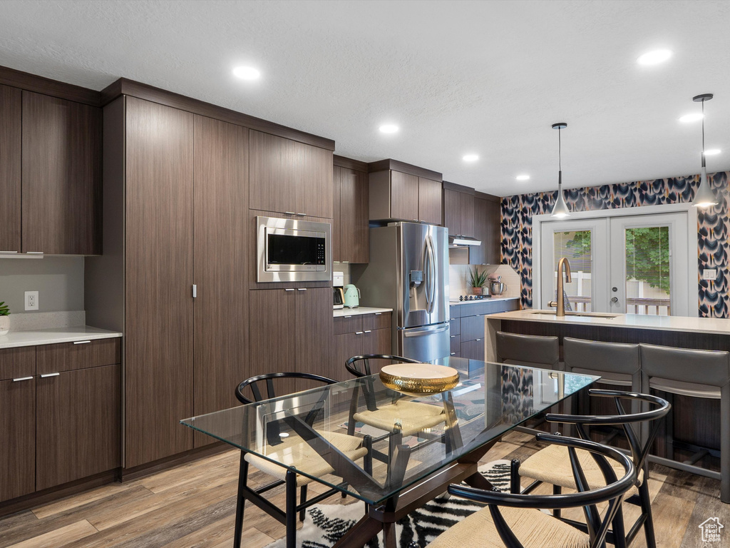 Kitchen featuring appliances with stainless steel finishes, light wood finished floors, hanging light fixtures, light countertops, and dark brown cabinets
