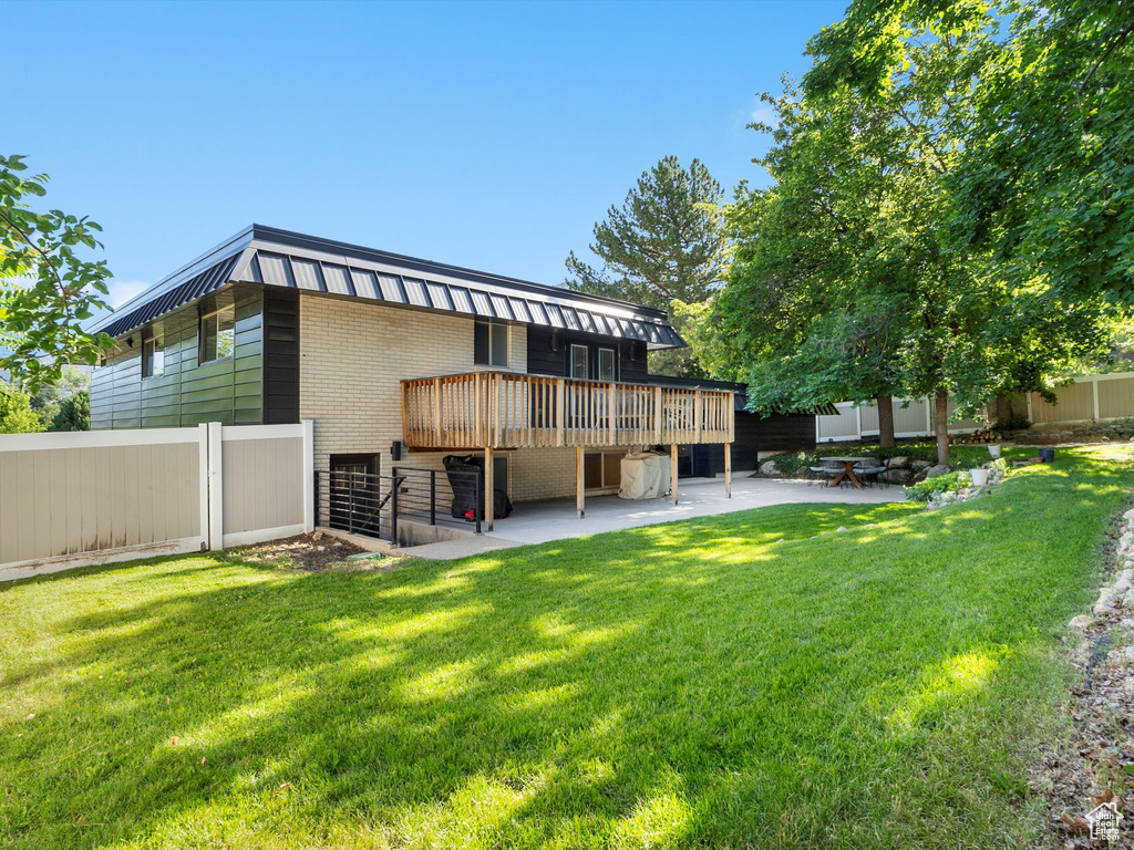 Rear view of property featuring a wooden deck, a patio area, brick siding, and mansard roof