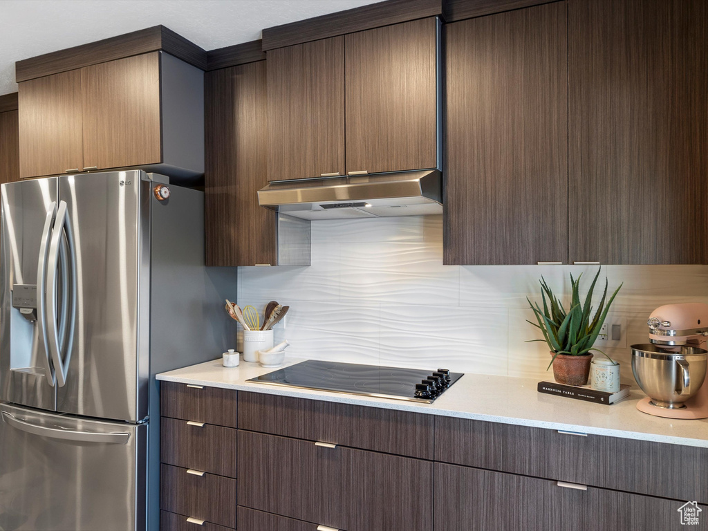 Kitchen featuring stainless steel fridge, black electric stovetop, range hood, decorative backsplash, and light countertops