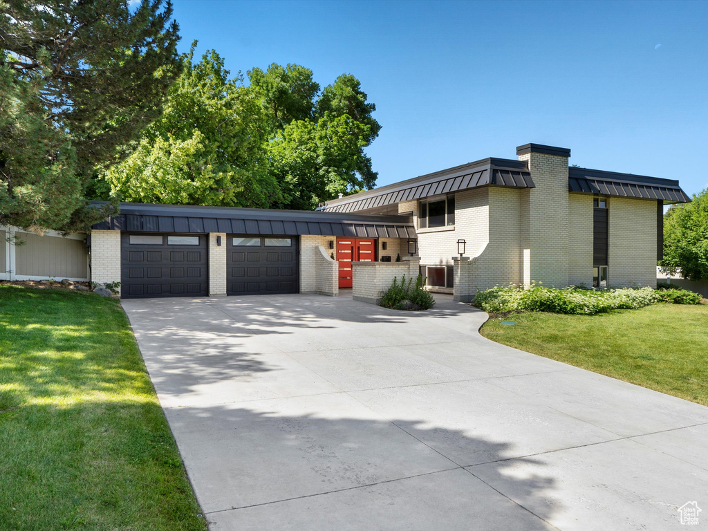 View of front of property with an attached garage, brick siding, concrete driveway, and a front lawn