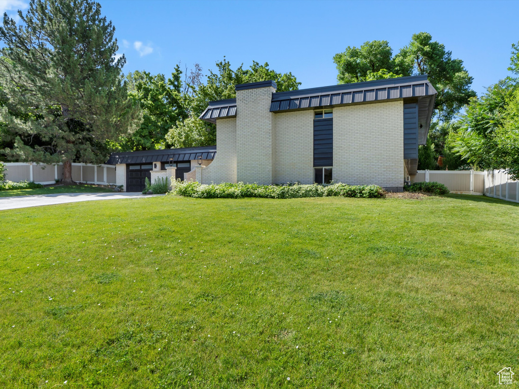 View of side of home with brick siding, a garage, concrete driveway, and a standing seam roof