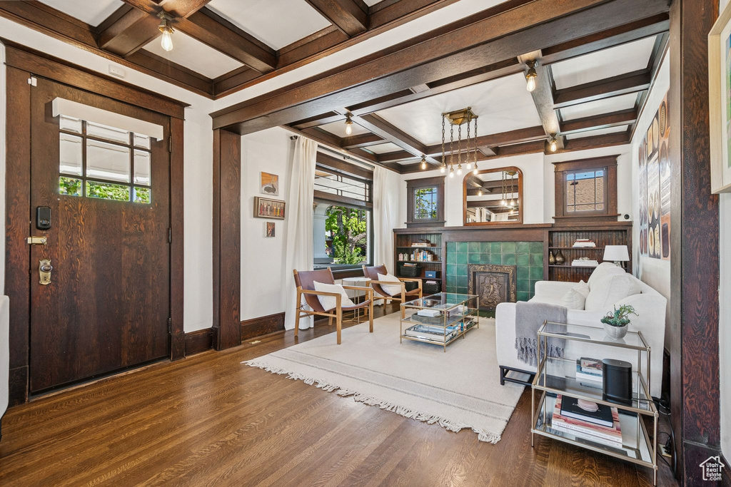 Living room with coffered ceiling, a tiled fireplace, wood finished floors, beamed ceiling, and a ceiling fan