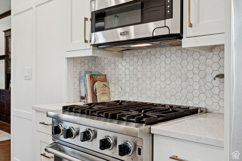 Kitchen featuring appliances with stainless steel finishes, decorative backsplash, white cabinetry, and light stone counters