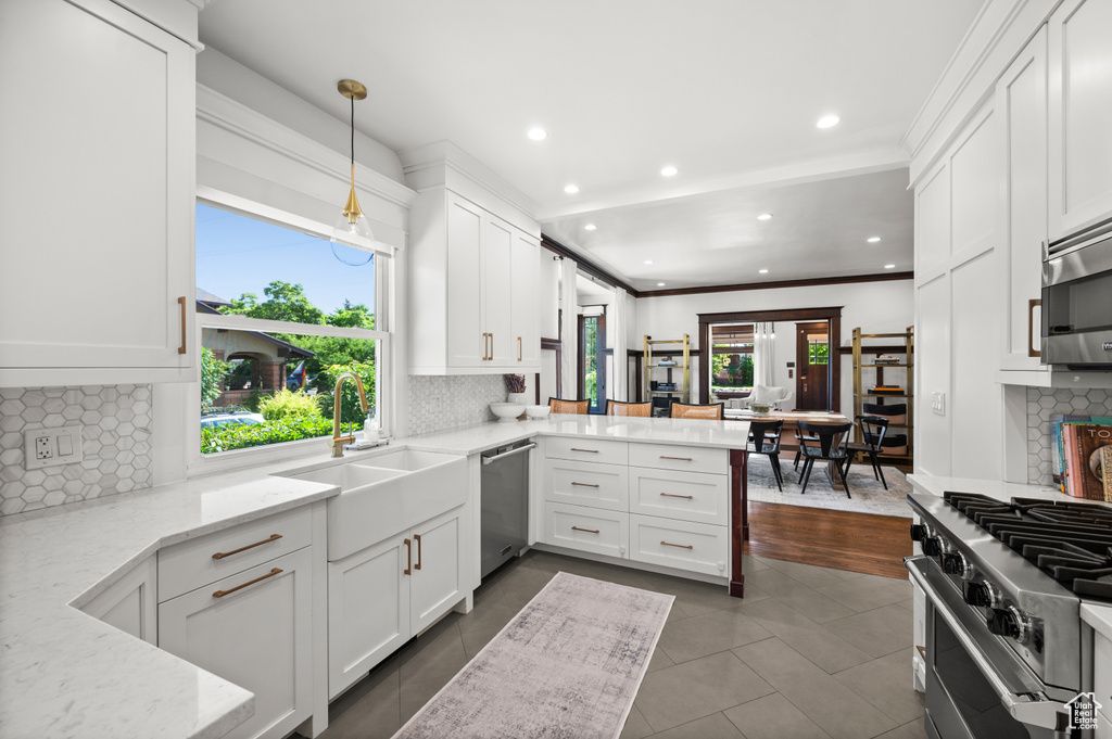 Kitchen featuring appliances with stainless steel finishes, a peninsula, white cabinetry, dark tile patterned flooring, and light stone countertops