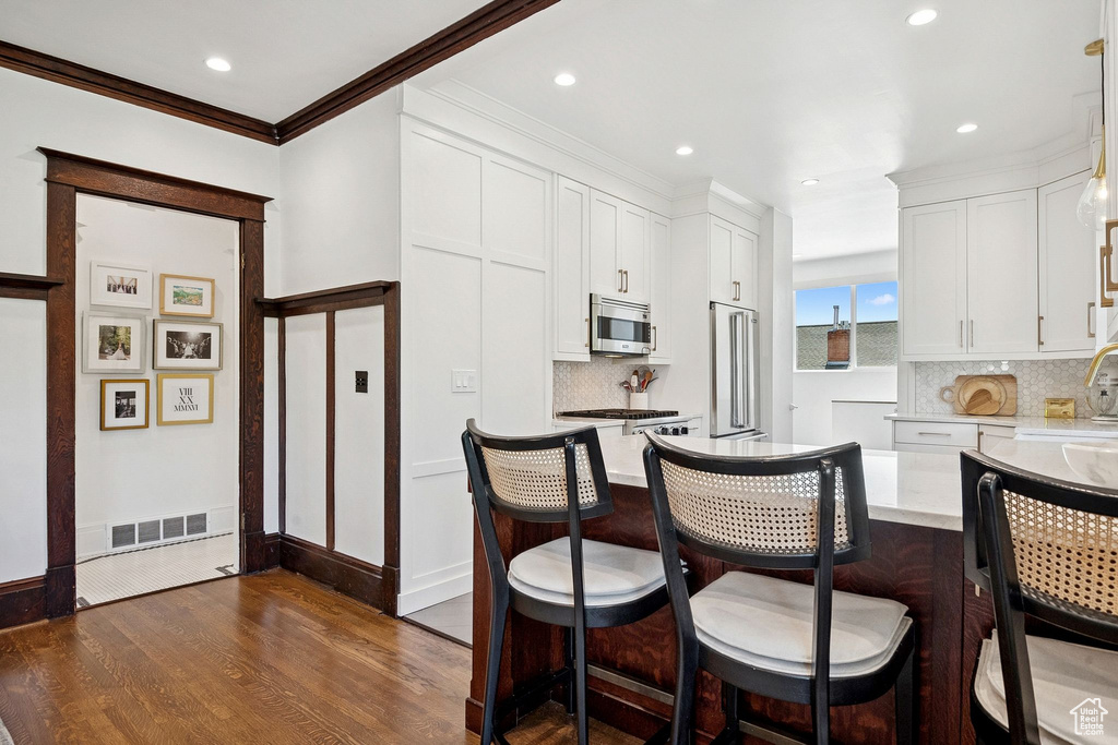 Kitchen featuring stainless steel microwave, dark wood finished floors, white cabinetry, backsplash, and crown molding