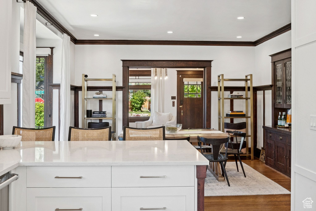 Kitchen with crown molding, plenty of natural light, wood finished floors, white cabinets, and recessed lighting